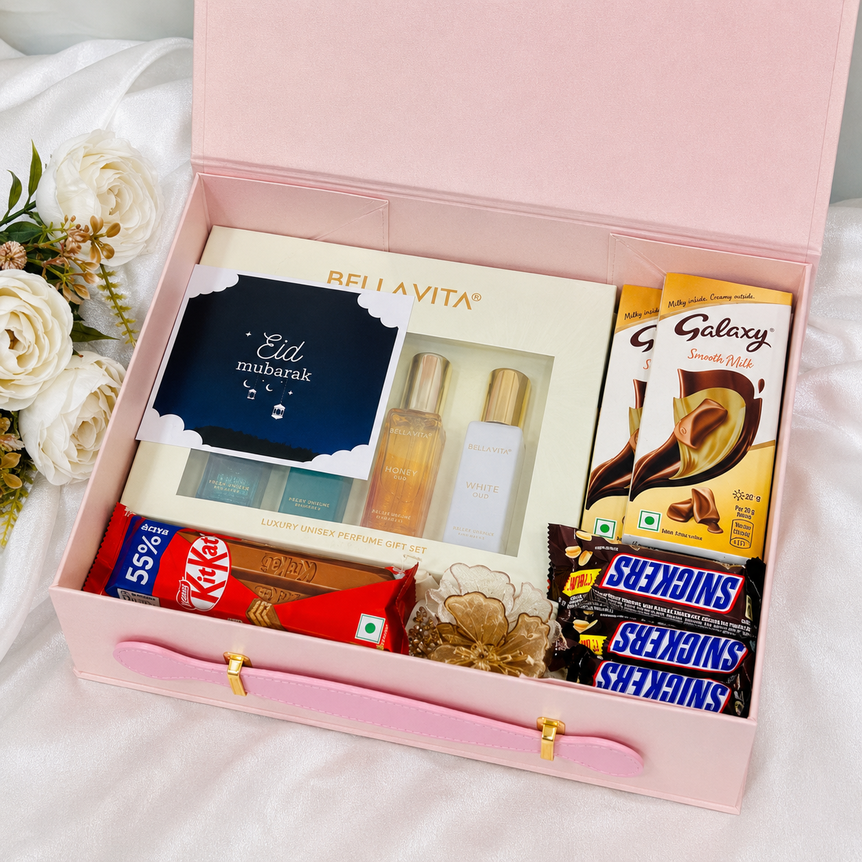 Luxury pink Eid gift hamper box with Bellavita perfume set, KitKat, Snickers, and Galaxy chocolates arranged in premium festive packaging