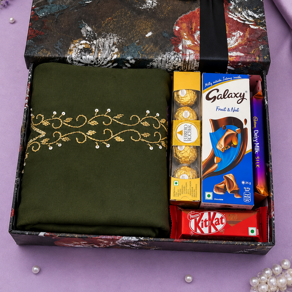 A luxury gift box set on a lavender background, featuring an olive green embroidered saree, Galaxy chocolate bars, KitKat, and Ferrero Rocher chocolates, and a decorative gift box with a black ribbon.