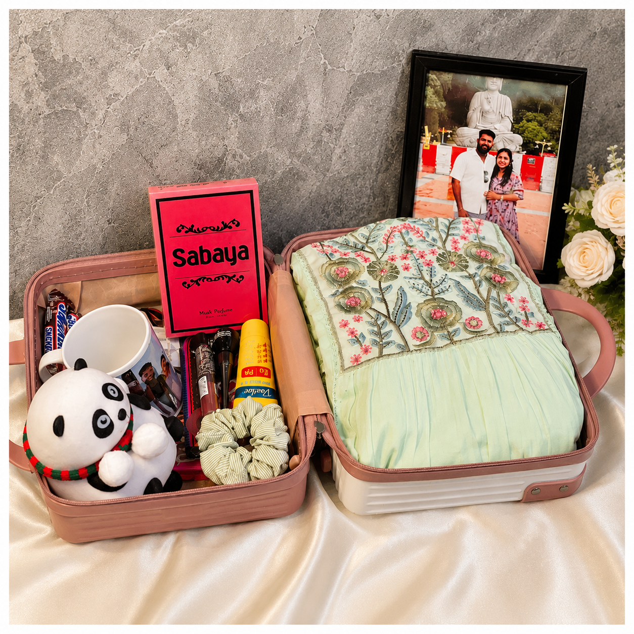 Premium women’s suitcase gift hamper with western dress, photo frame, perfume, panda soft toy, coffee mug, chocolates, sunscreen, eyeliner, lipstick and hair accessories.