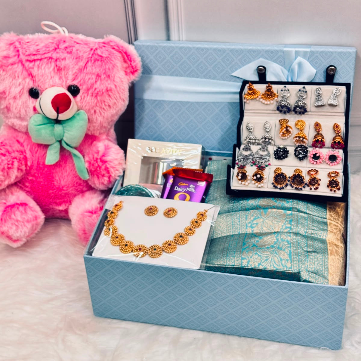 Luxury birthday gift hamper with Davani, necklace set, 12 pairs of earrings, Kuppivala bangles, perfume, teddy bear, Dairy Milk chocolates, and premium blue gift box by Miravie