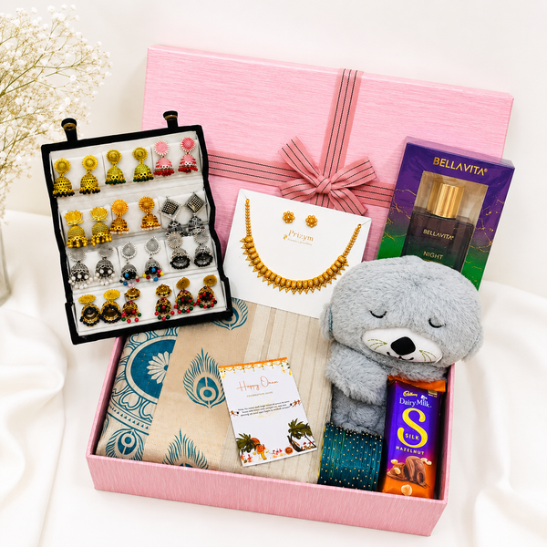 Premium Onam gift hamper featuring a traditional saree, temple jewellery set, jhumka earrings collection, decorative bangles, Bella Vita perfume, Dairy Milk Silk chocolate, teddy bear, greeting card, and luxury pink gift box.